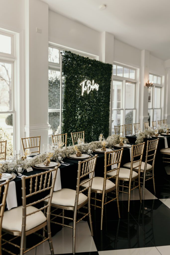 wedding reception banquet table with gold accents and a neon last name sign.