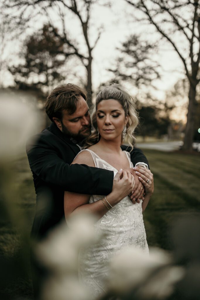 Groom holding bride with ponytail and classic makeup.