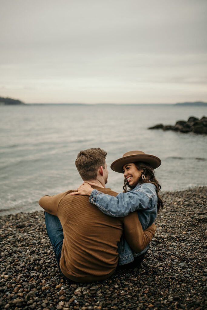 engaged couple sitting on the beach watching the waves of the puget sound for their adventure session