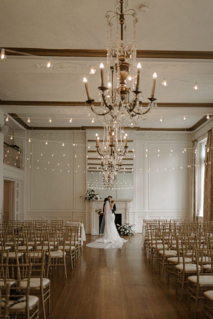 bride-and-groom-in-front-of-white-fireplace-with-string-lights-and-florals