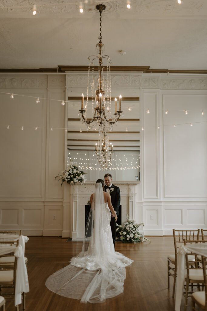 bride-and-groom-in-front-of-white-fireplace-with-string-lights-and-florals