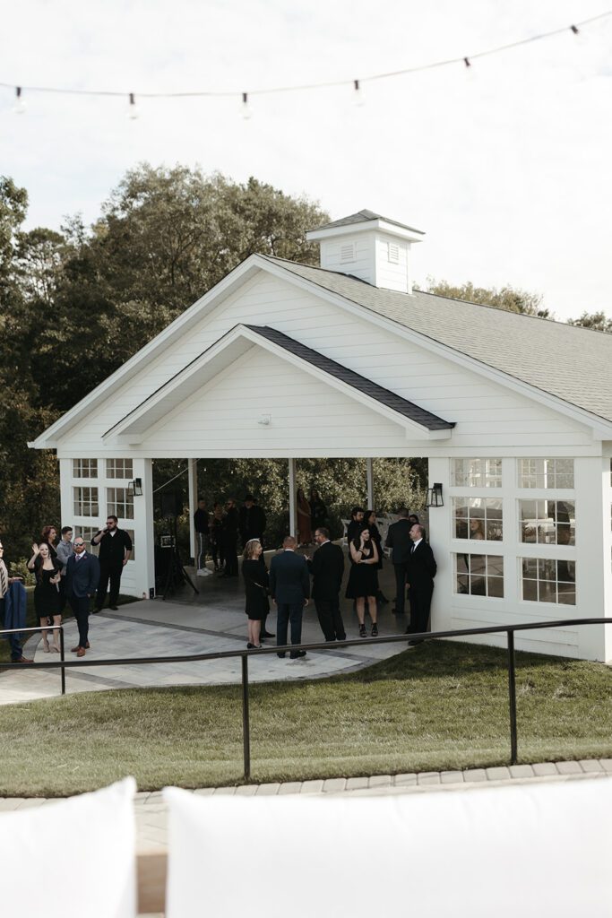 guests-gather-on-patio-before-white-barn-wedding-ceremony